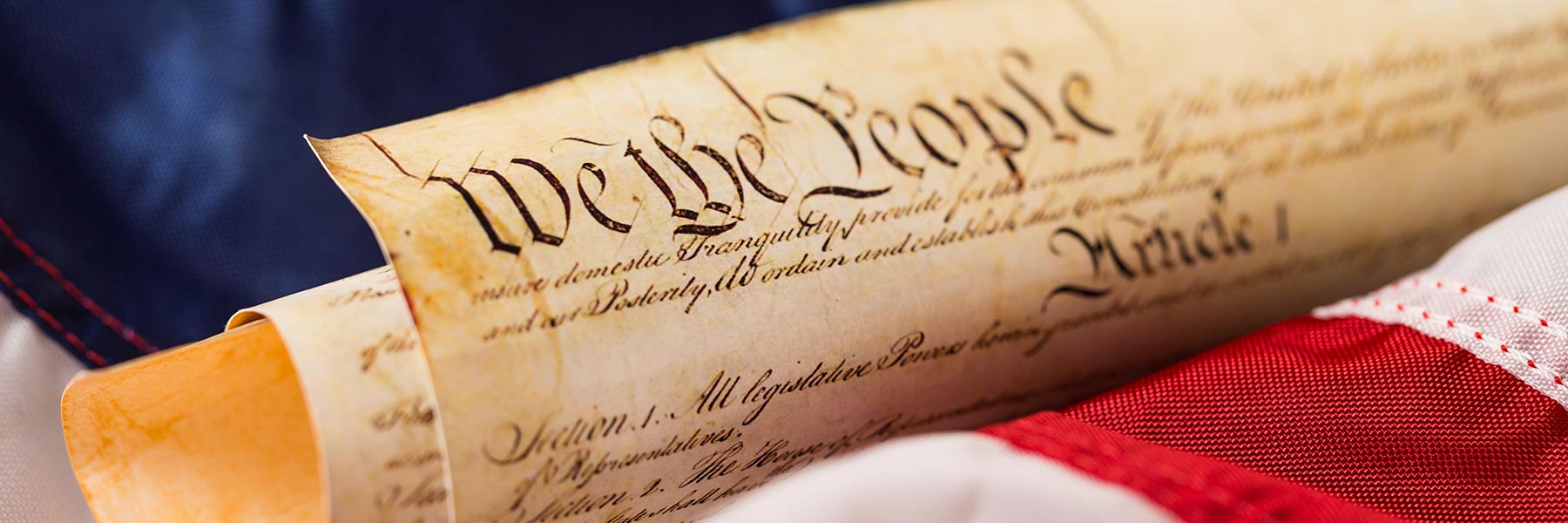 Printed copy of the Constitution rolled up and laid on top an American flag.