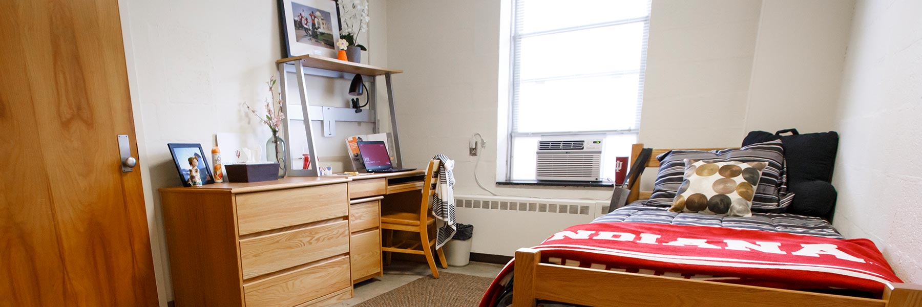 View into a student housing room with bed, desk, chair and other items.