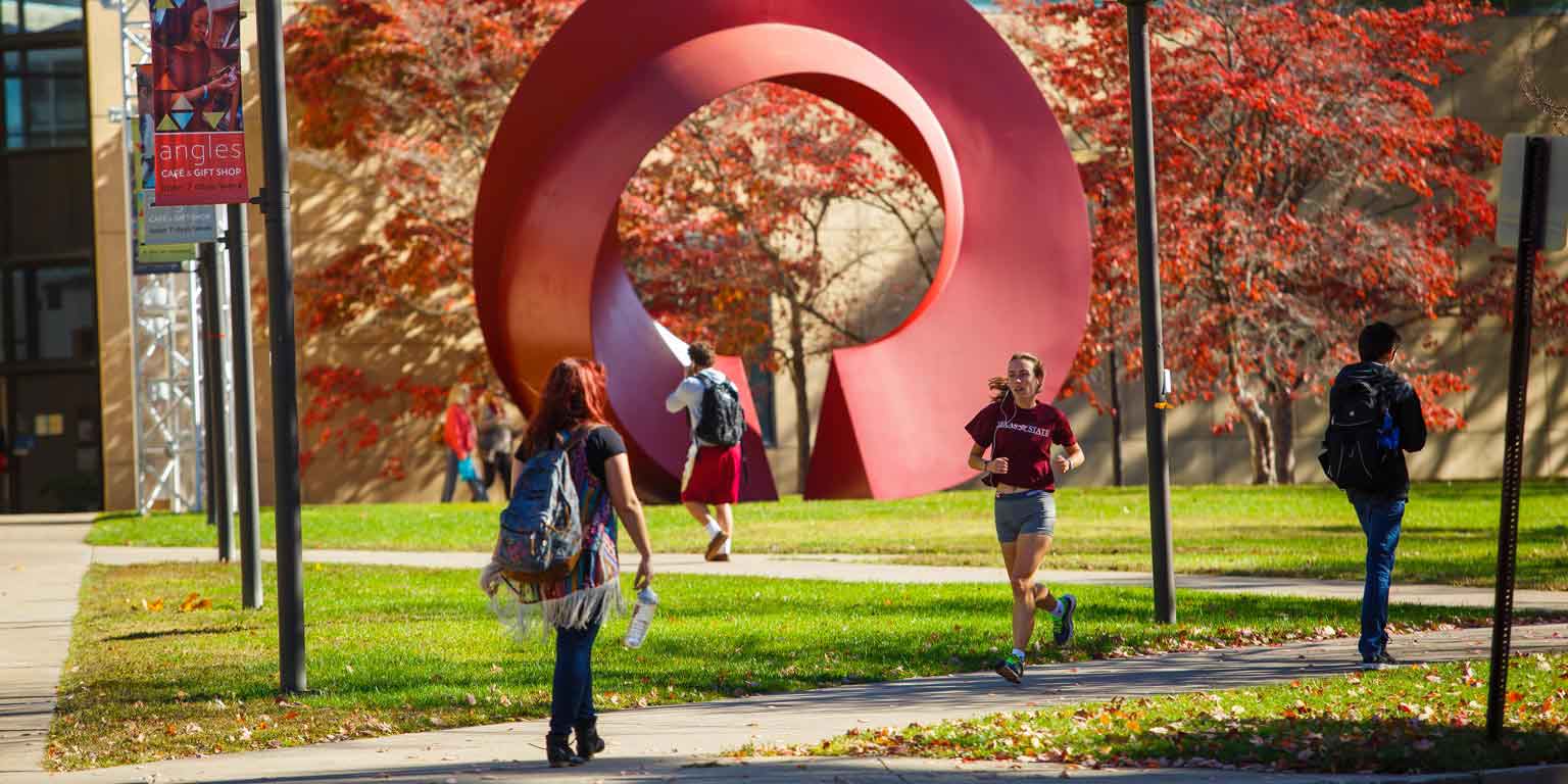 Students walk along paved paths outside the Ezkenazi Art Museum on a fall day.